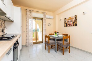 A kitchen with a stove, oven, and dishwasher, a dining table with chairs, a sliding glass door, and a wall-mounted clock.