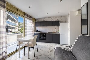 A modern kitchen with dark cabinets, a white refrigerator, and a dining area with a table and chairs. - Apartment 'Proche Croisette' with Balcony, Wi-Fi and Air Conditioning (Cannes)