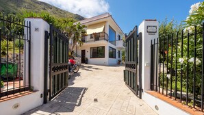 A gated entrance to a modern two-story house with a balcony, a motorcycle parked in front, and a mountain in the background. - Villa 'Anna Messina' with sea view, Wi-Fi and air conditioning (Carini)