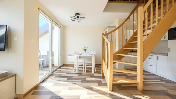 Une cuisine moderne avec un escalier en bois, un coin repas avec une table et des chaises, et une grande porte-fenêtre coulissante donnant sur un espace extérieur.