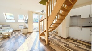 Un salon moderne avec un escalier en bois, une table basse en verre et un coin cuisine doté de meubles blancs.