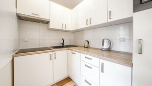 Une cuisine moderne avec des meubles blancs, un plan de travail en bois, une bouilloire en acier inoxydable et un robinet noir.