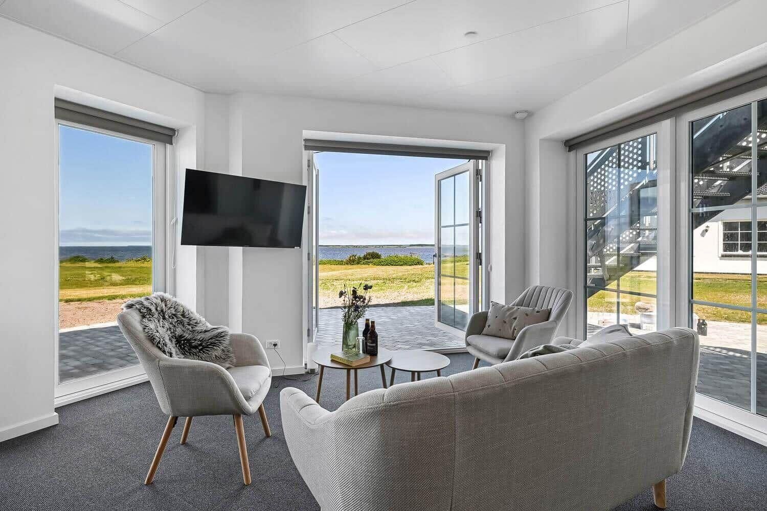 Ein modernes Wohnzimmer mit großem Fernseher, bequemen Sitzmöglichkeiten, einem kleinen Tisch und Blick ins Freie.