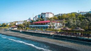Ένα παραθαλάσσιο ξενοδοχείο με θέα στη θάλασσα, έναν παραλιακό πεζόδρομο και κτίρια στο βάθος.
