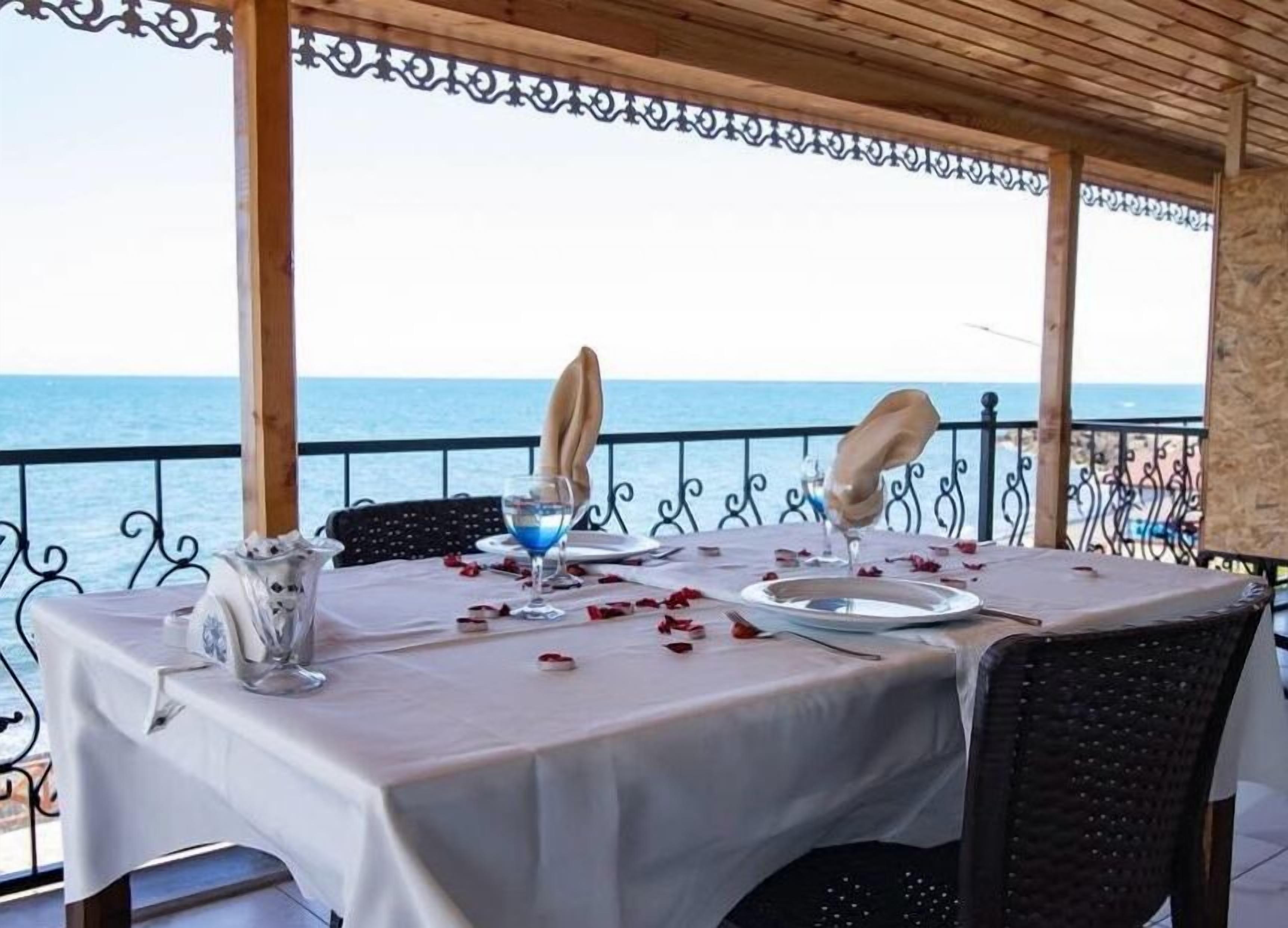Mesa para dos con vista al mar, mantel blanco y barandilla metálica decorativa.