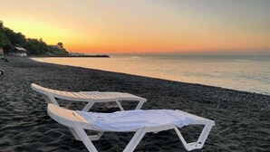 Μια παραλία με δύο λευκές ξαπλώστρες και μια λευκή πετσέτα στην άμμο.