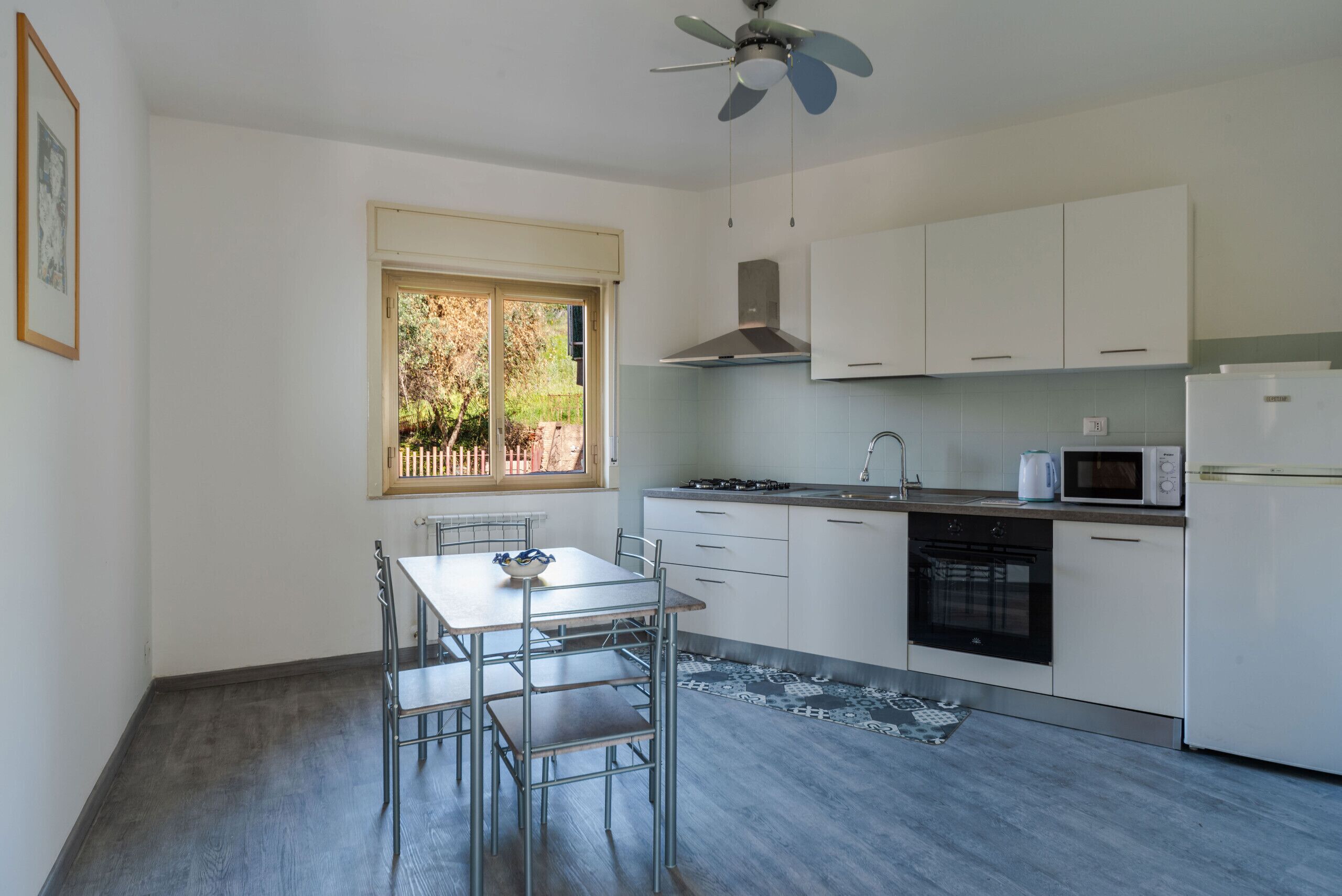 Una cucina moderna con mobili bianchi, piano cottura a gas, forno a microonde ed elettrodomestici inclusa la lavastoviglie. Si trova una tavola con sedie e un ventilatore a soffitto.