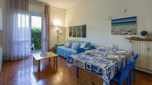 Un comedor con una mesa dispuesta para cuatro personas, un sofá y un cuadro de una escena de playa.