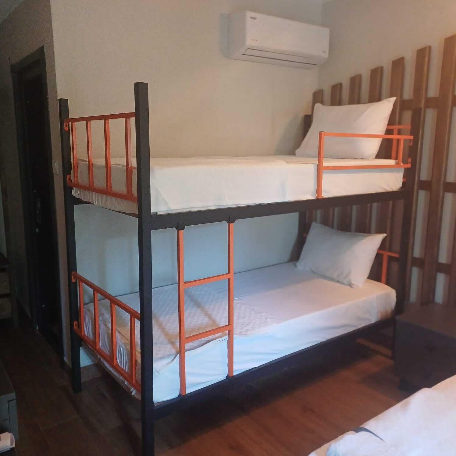 A bunk bed with a white mattress and orange railings, an air conditioning unit above, and a wooden panel wall.