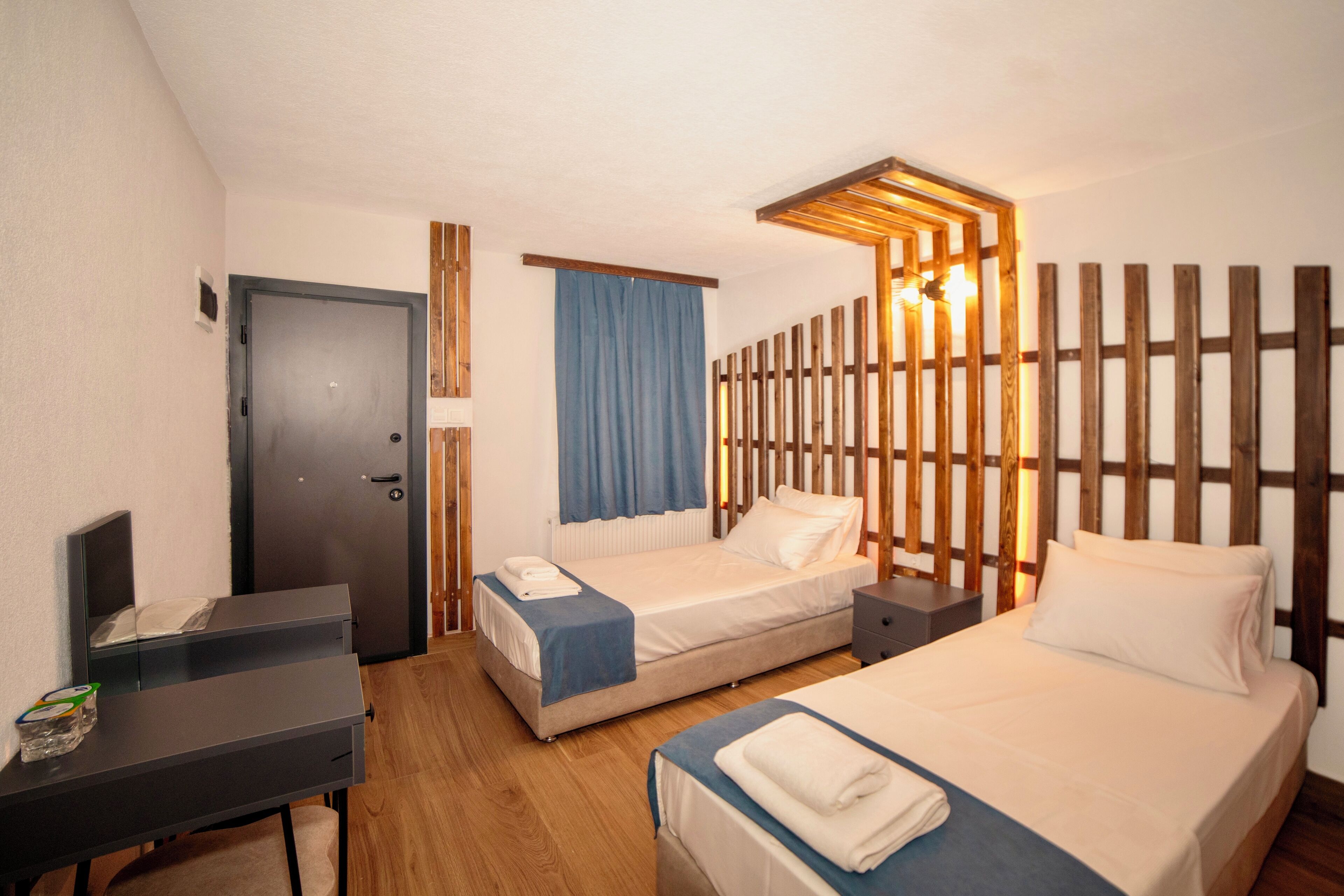 Ett hotellrum med två sängar, ett skrivbord, en garderob och en väggavdelare i trä med inbyggda lampor.
