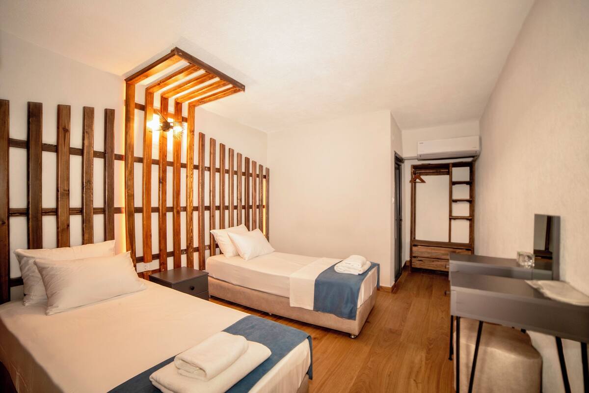 Ein Hotelzimmer mit zwei Betten, einem Schreibtisch und einem Bettgestell aus Holzlamellen.
