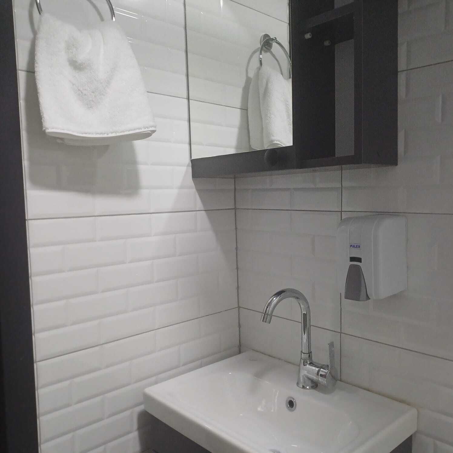 A bathroom with white tiled walls, a white sink, a mirror, and a towel rack with two towels.