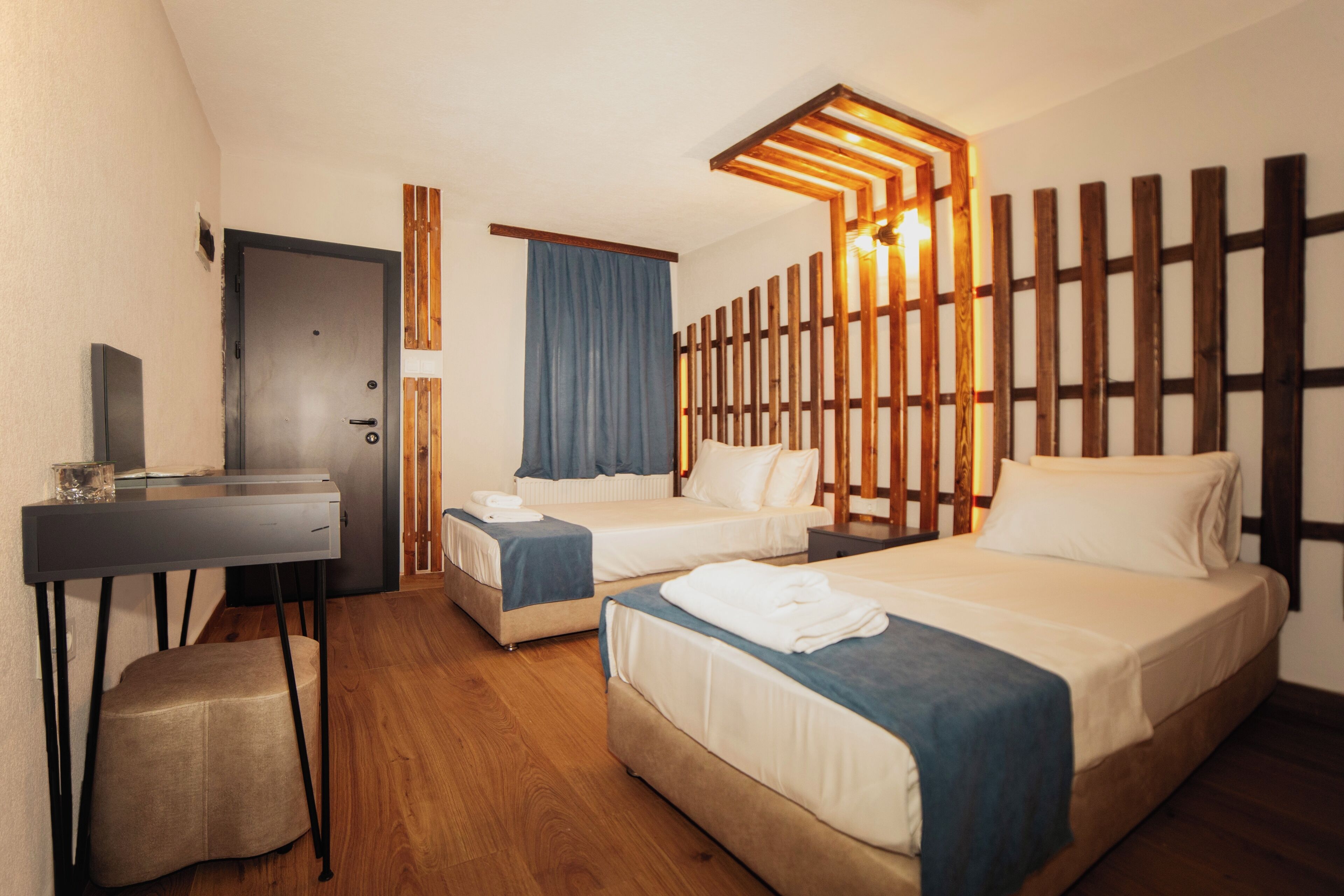 A hotel room with two beds, a desk, a chair, and a wooden partition with lights.