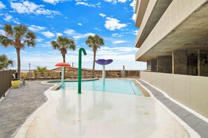 Una piscina con cielo azul despejado, palmeras y un edificio de concreto al fondo.