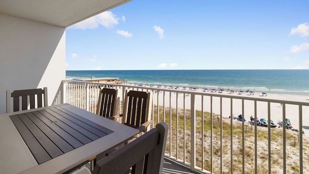 Ein Balkon mit Tisch und Stühlen mit Blick auf einen Strand, auf dem sich Menschen und Boote befinden.