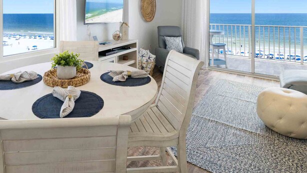 Un salon moderne doté d’un grand téléviseur, d’un coin repas avec une table et des chaises, et d’un balcon offrant une vue sur la plage.