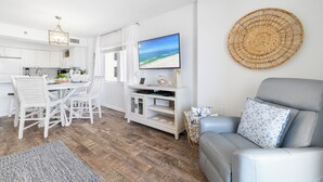 Un salon moderne avec un canapé gris, un coin repas avec des chaises blanches et une cuisine avec des meubles blancs.
