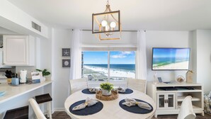 Un coin repas avec une table ronde, des chaises, un lustre, un téléviseur et une vue sur la plage.