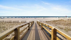 Une promenade en bois menant à une plage, avec un ciel dégagé.
