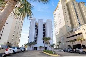 Hotel de vários andares com entrada central, estacionamento e palmeiras.