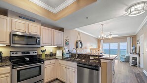 A modern kitchen with stainless steel appliances, wooden cabinets, and a view of the ocean. - Crystal Tower 1606 by Liquid Life (Gulf Shores)