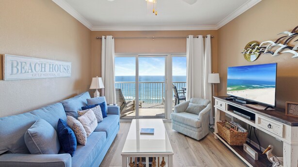 A living room with a sofa, coffee table, TV, and a balcony with a view of the ocean. - Crystal Tower 1606 by Liquid Life (Gulf Shores)