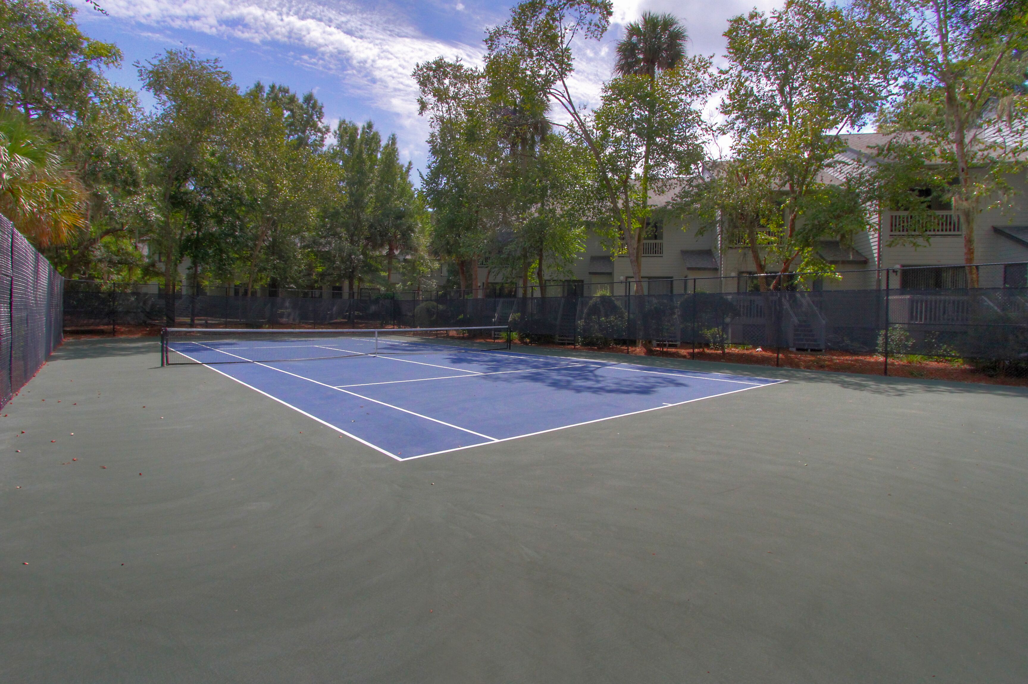 An outdoor tennis court surrounded by trees and a building.