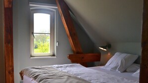A bedroom with a sloped ceiling, a window with a view of greenery, a bedside lamp, and a bed with white linens. - Double room in the Gasthaus am Finowkanal (former school from 1875). (Wandlitz)