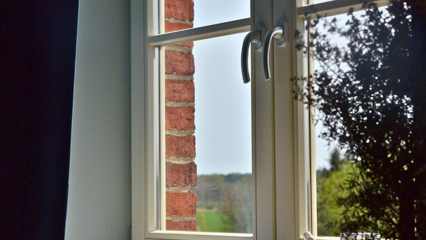A window with a view of a brick wall and greenery outside. - Double room in the Gasthaus am Finowkanal (former school from 1875). (Wandlitz)