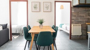 A compact living space with a wooden dining table, green upholstered chairs, a small potted plant, and a bed with a white blanket. - Downtown Apartment ° 2 bedrooms ° near the Arènes ° air conditioning  (Nîmes)