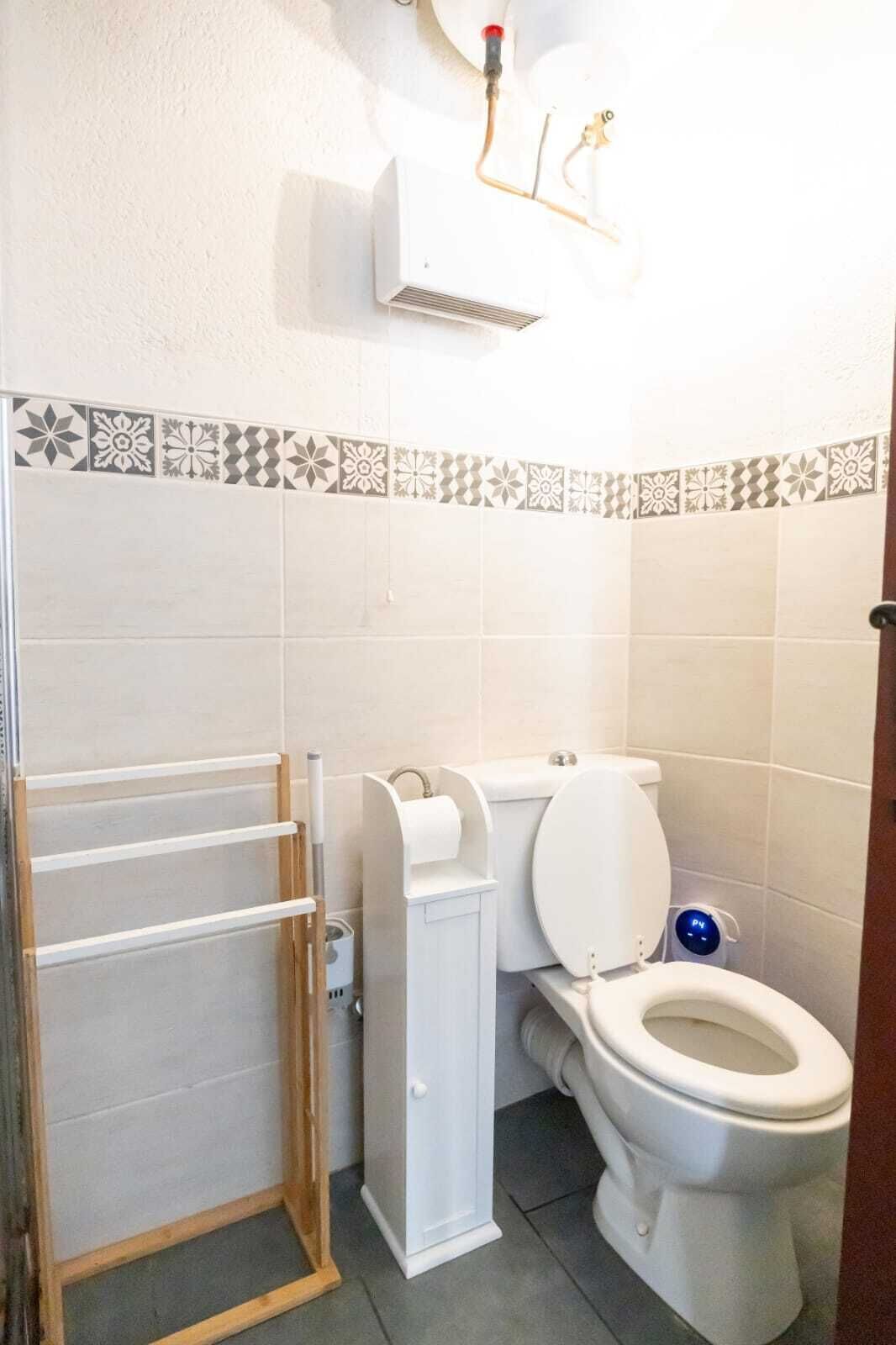Un baño con inodoro, secamanos, toallero y cabezal de ducha.