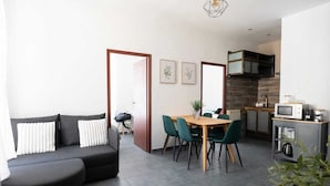 A modern living room with a sofa, a dining table with chairs, a kitchen area with appliances, and a staircase. - Downtown Apartment ° 2 bedrooms ° near the Arènes ° air conditioning  (Nîmes)