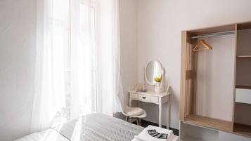 Un dormitorio con cama, mesita de noche con espejo, una silla y un armario.