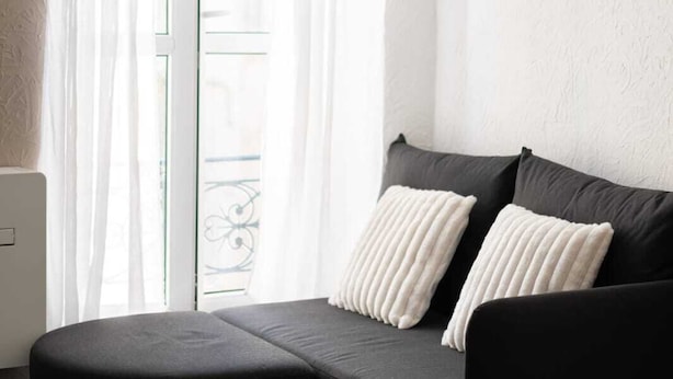 A corner sofa with two white pillows, a dark ottoman, and a view of a balcony through a glass door. - Downtown Apartment ° 2 bedrooms ° near the Arènes ° air conditioning  (Nîmes)