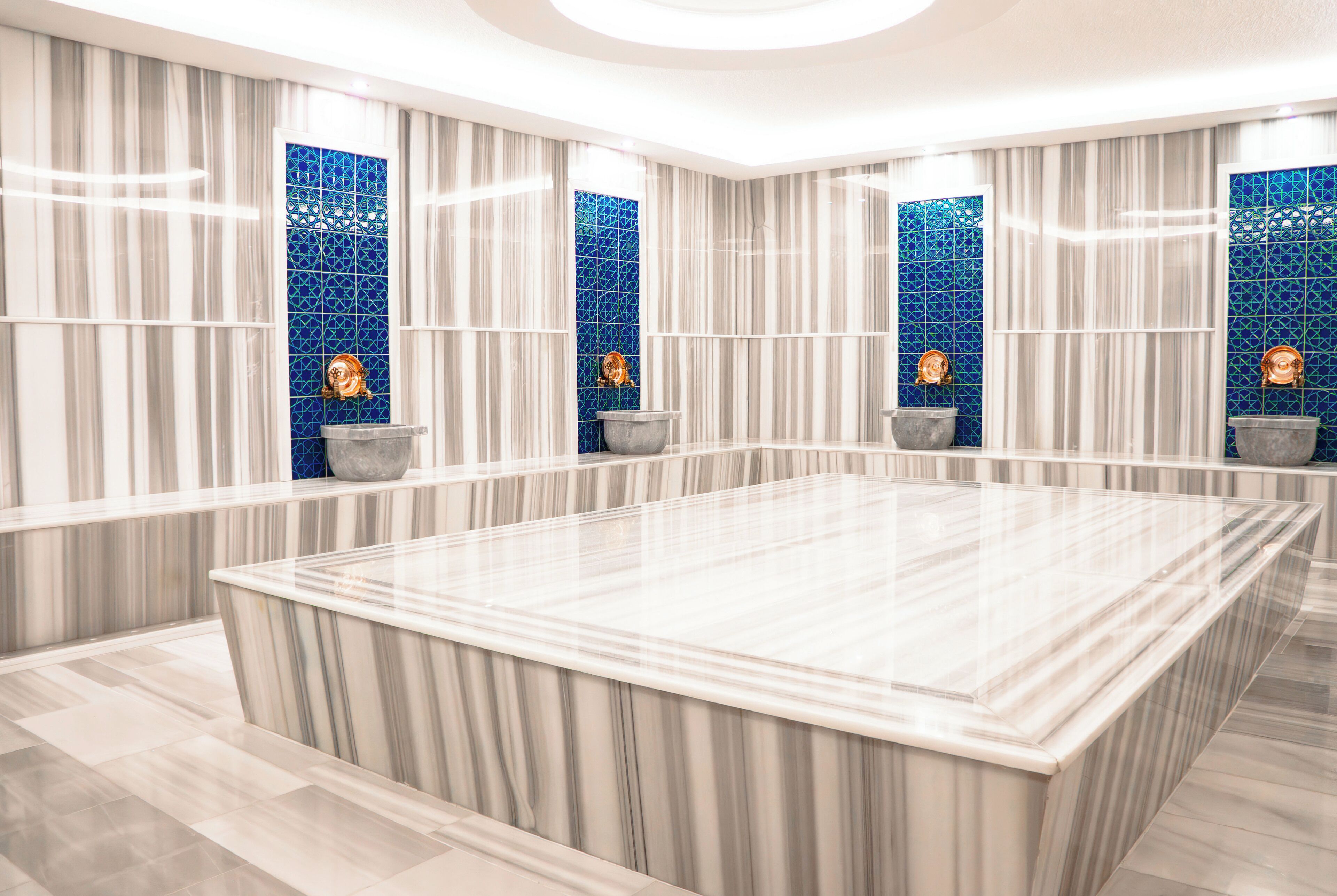 Un baño moderno con un amplio tocador de mármol, azulejos de mosaico azul y dos jarrones decorativos.