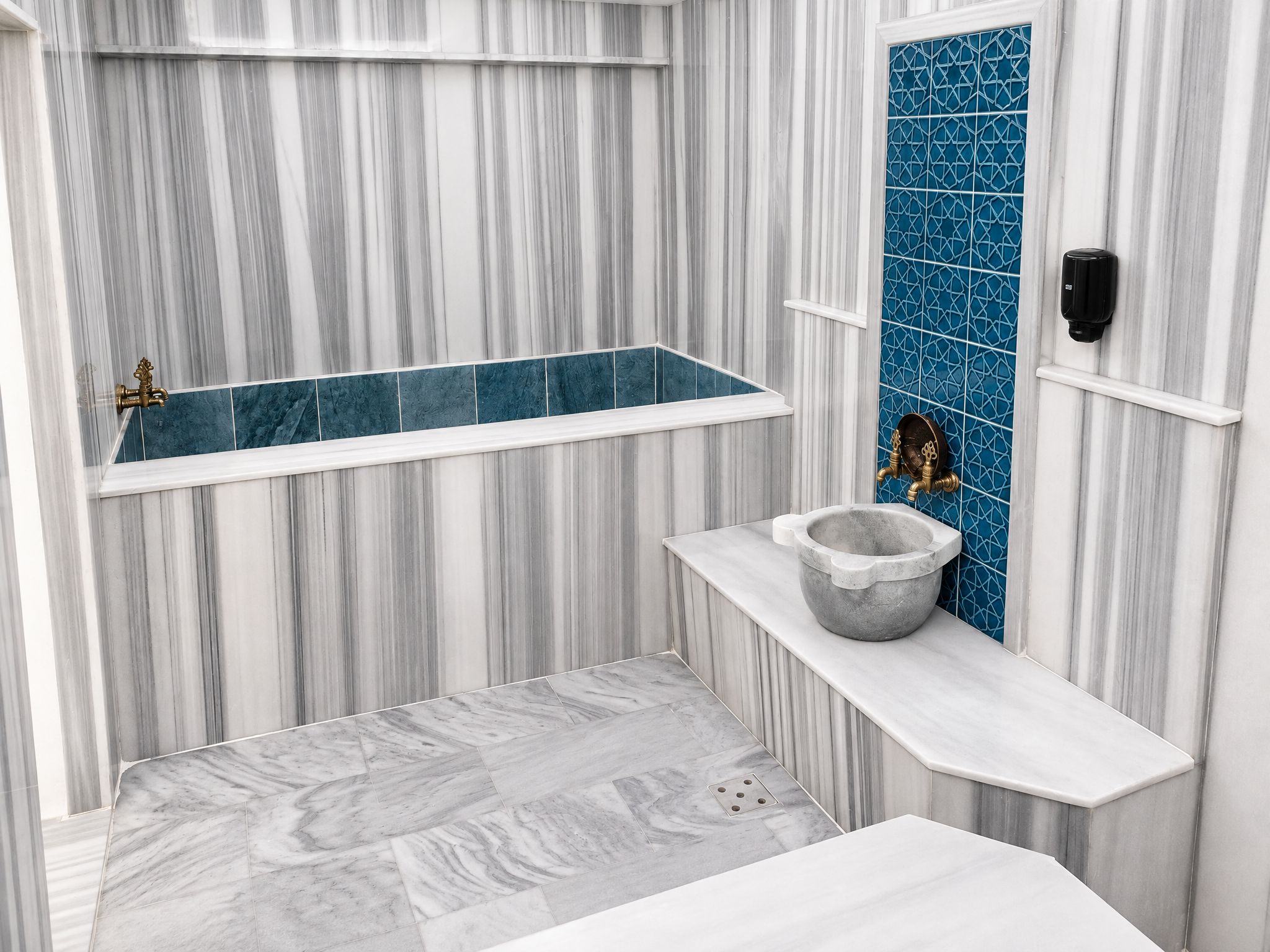 A bathroom with a marble vanity, a bathtub with blue tiles, and a stone basin.