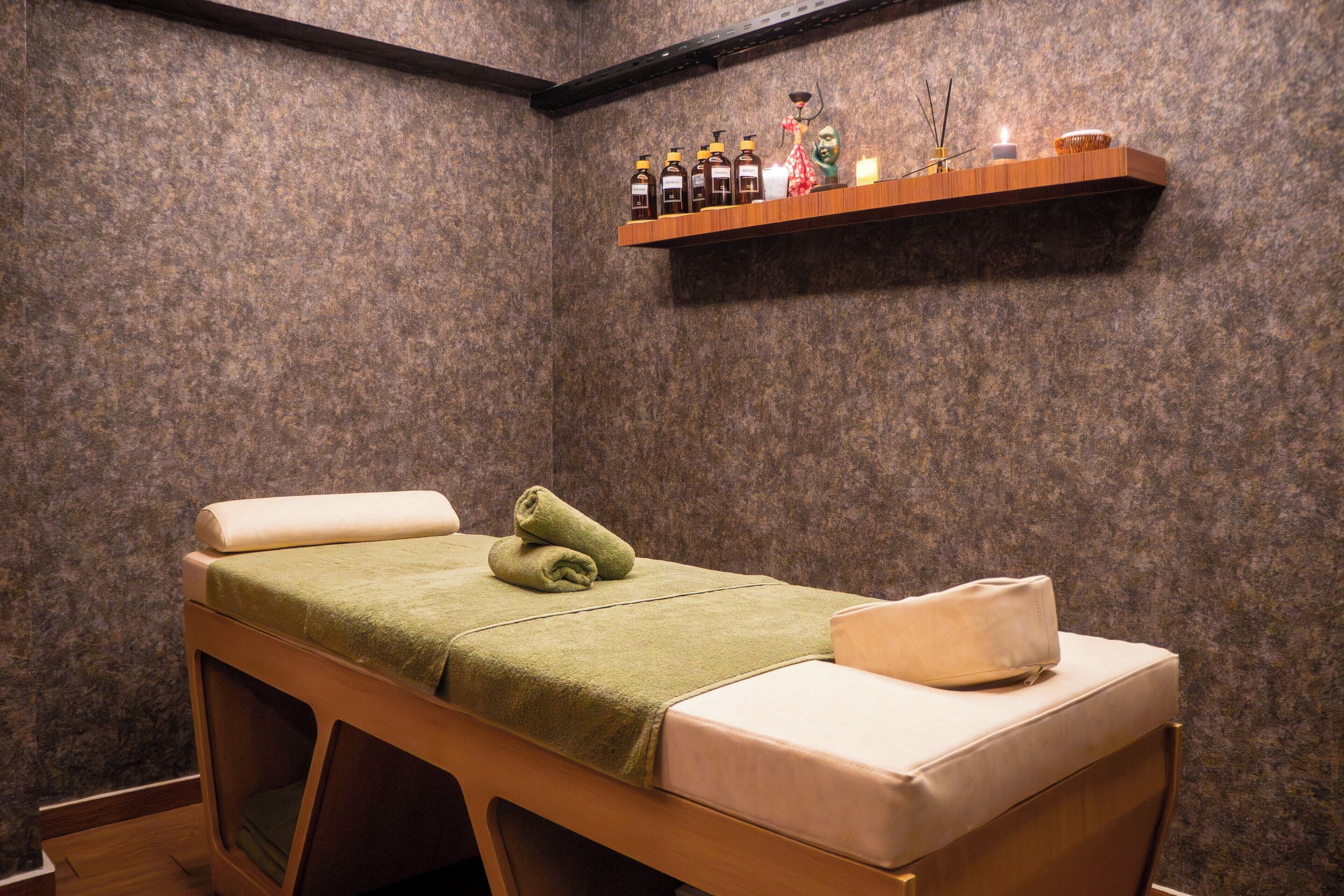 A massage room with a wooden bed, a shelf with bottles, and a candle.