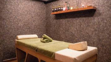 A massage room with a wooden bed, a shelf with bottles, and a candle.