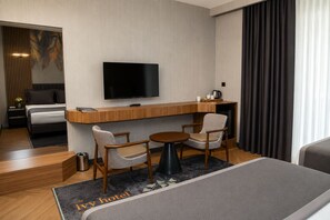 A hotel room with a bed, a desk with a flat-screen TV, two chairs, a small table, and a coffee machine. - ivy Hotel Spa (Cinarcik)