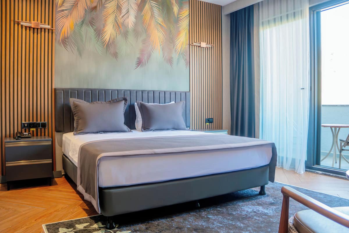 A modern hotel room with a large bed, a nightstand, a coffee machine, and a view of the sea through large windows.