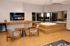 A modern hotel room with a TV displaying Google TV, a wooden vanity with a sink, and two chairs. - ivy Hotel Spa (Cinarcik)