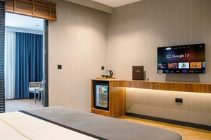 A hotel room with a bed, a small seating area, a minibar, and a mounted TV displaying Google TV. - ivy Hotel Spa (Cinarcik)