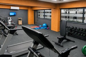 Un gimnasio con equipo de ejercicio, un televisor y una ventana con ilustraciones de ejercicios.