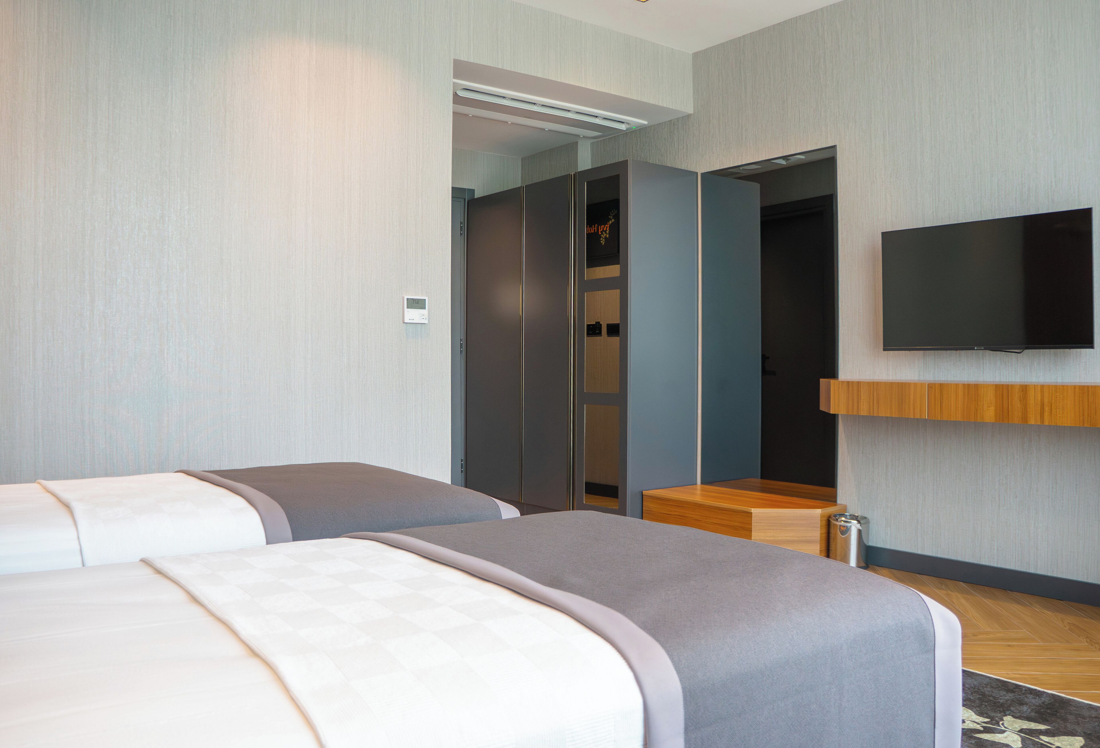 Habitación de hotel con dos camas, un televisor montado en la pared y un banco de madera.