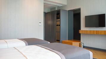 Habitación de hotel con dos camas, un televisor montado en la pared y un banco de madera.