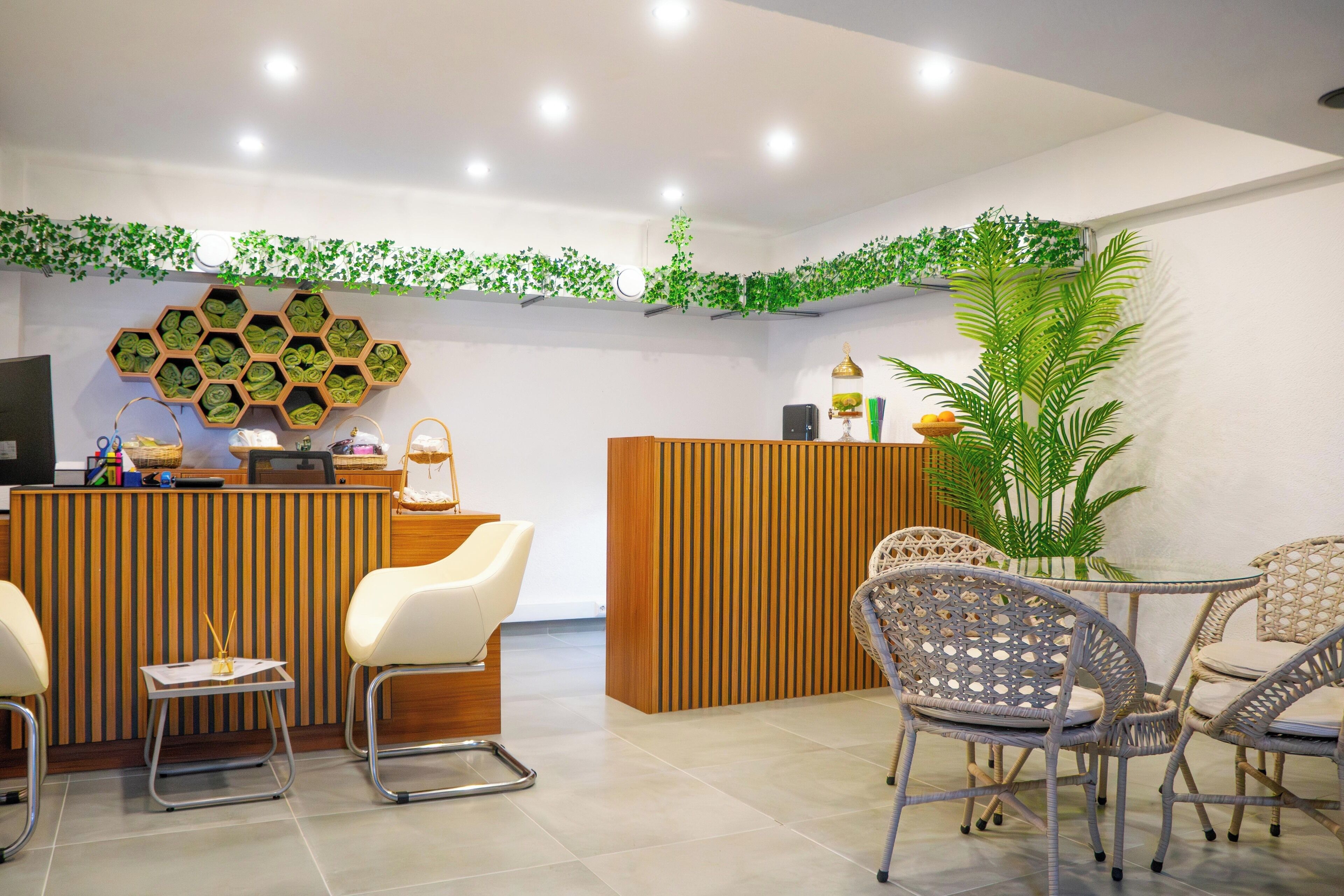 A reception area with a wooden reception desk, two white chairs, wicker chairs around a small table, and a large potted plant.