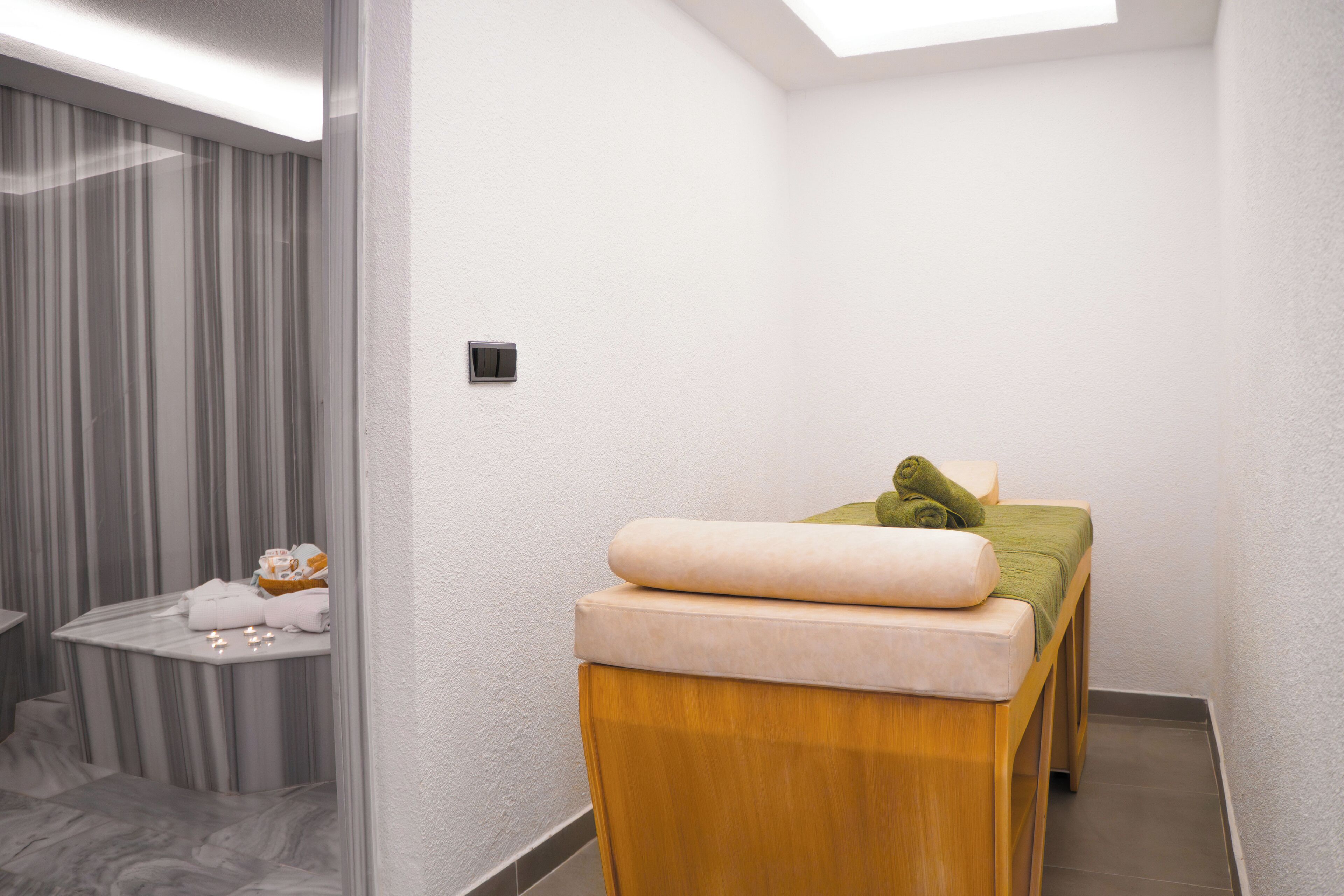 A modern spa room with a massage table, a small table with towels, and a curtain-covered window.