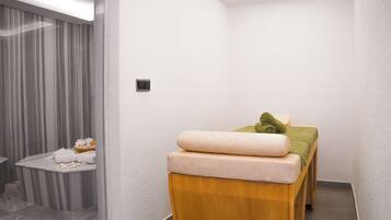 A modern spa room with a massage table, a small table with towels, and a curtain-covered window.