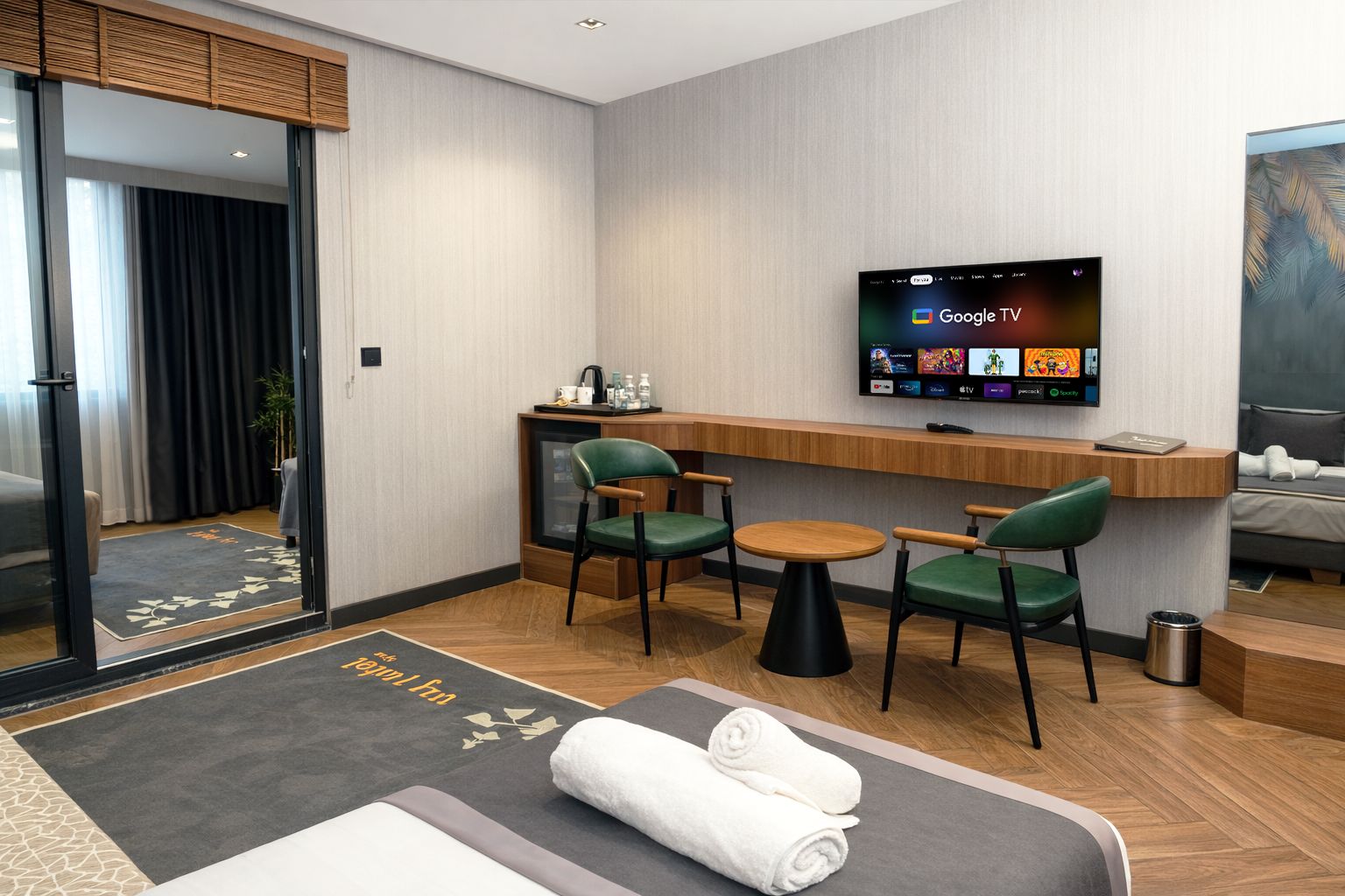 Una habitación de hotel con cama, escritorio con silla, televisor montado en la pared y una mesita.
