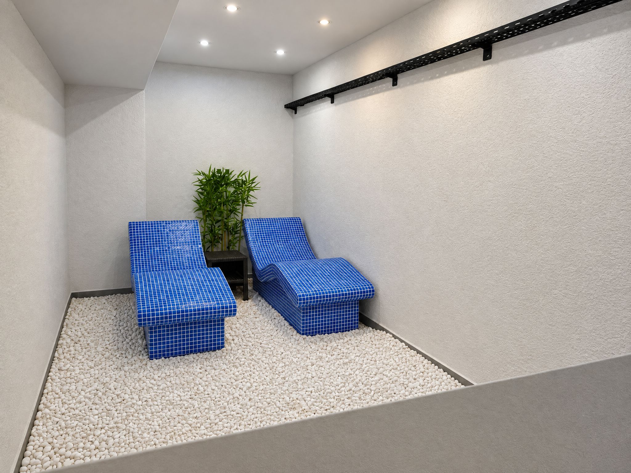 A spa room with two blue cushioned chairs, a small plant, and a pebble floor.